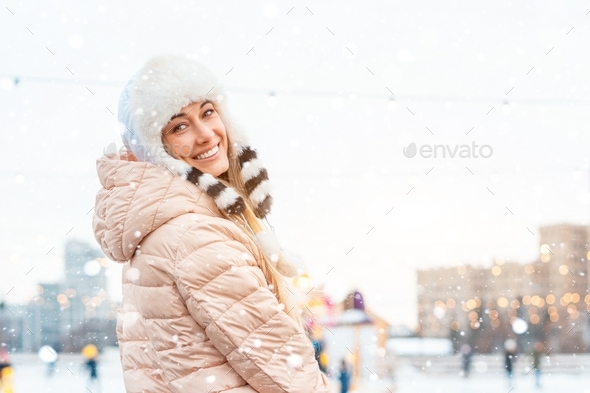 Woman in fluffy fur hat winter jacket standing outdoor near ice skating rink. Christmas mood
