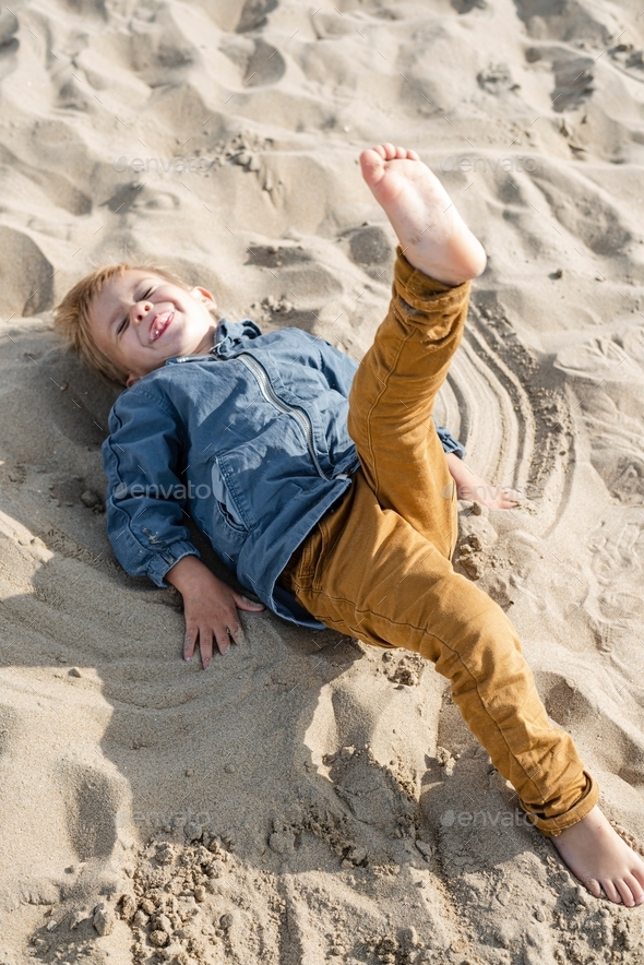Little boy makes a sand angel on the beach.