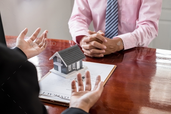 A real estate agent with a home model is talking to clients about renting a home and buying home  - Stock Photo - Images