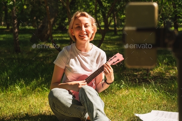 Cute teenage girl playing ukulele in front of the camera. Online music lessons.