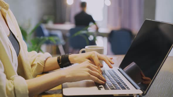 Woman Types on Laptop at Workplace Against Blurry Colleague