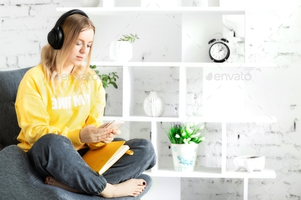 Girl in earphones in yellow blouse sit relax on grey couch use smartphone