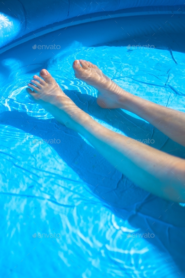 Human woman female legs in blue water inflatable pool relaxing summer feet