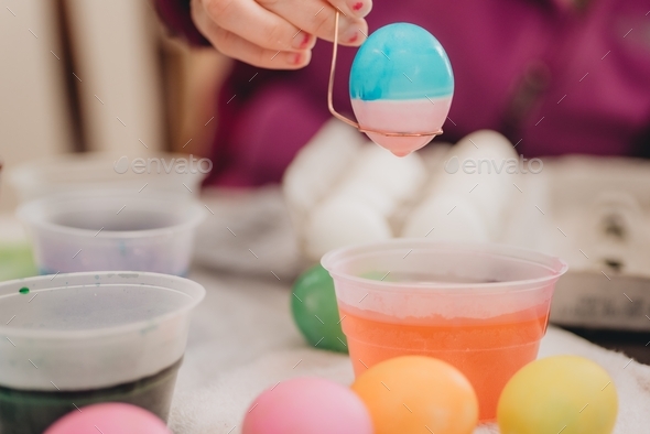 Young millennial Mother at home helping daughter paint colorful Easter eggs for playing and eating - Stock Photo - Images