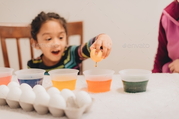 Young diverse pre school age girl at home painting Easter eggs with mother - Stock Photo - Images