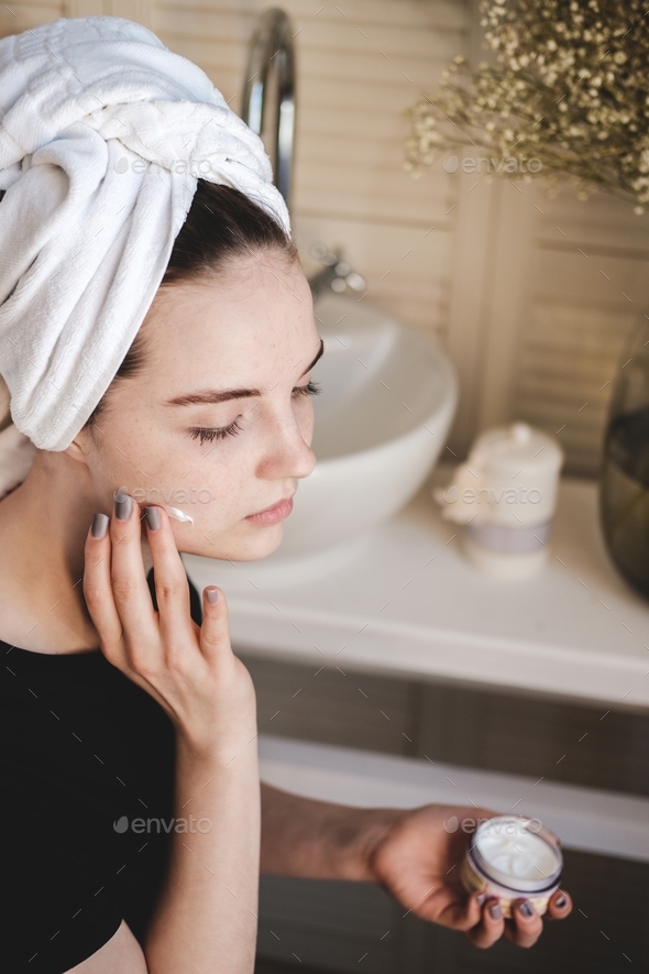 After a shower, a young girl with freckles applies sunscreen