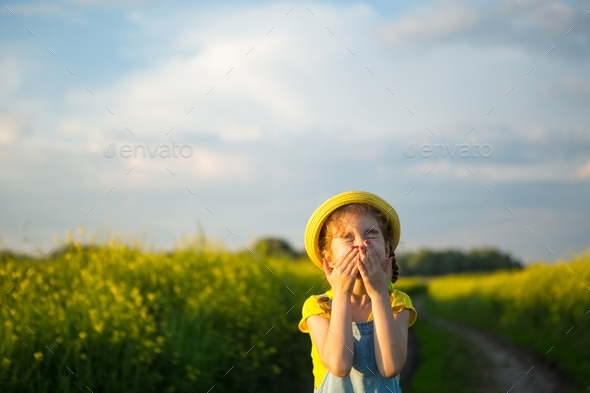 The girl in the yellow blooming field covered her nose and face with her hands and wrinkled up