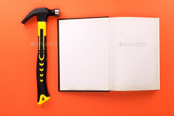 Top view shot of open book with blank pages and hammer on orange surface