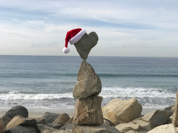 Rocks are balanced at the beach with a Santa hat