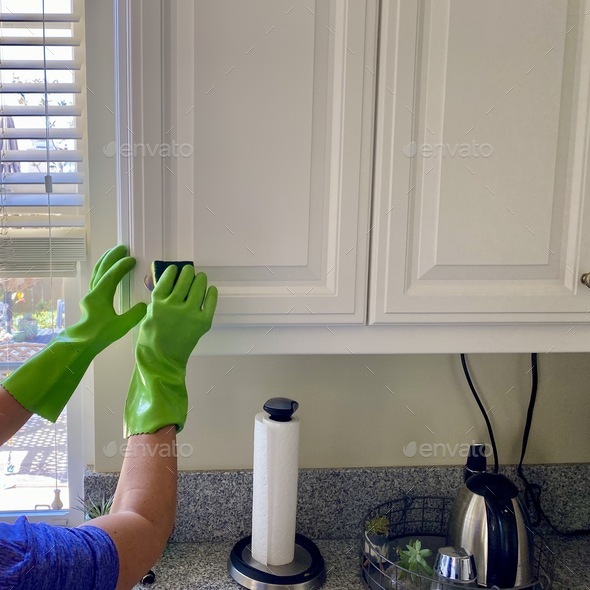 A woman wipes the cabinets clean and disinfects with rubber gloves