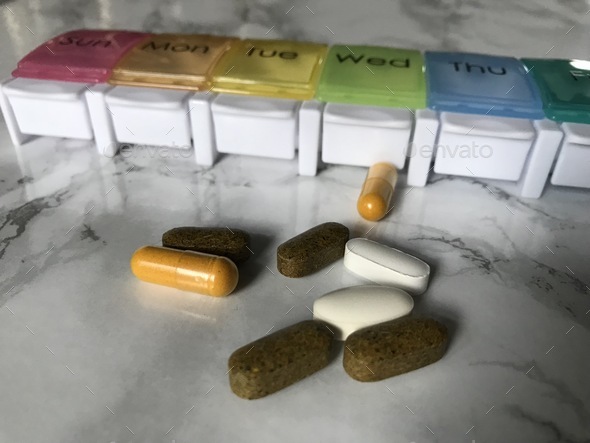 Prenatal vitamins and other supplements sit on a marble counter next to a pill container