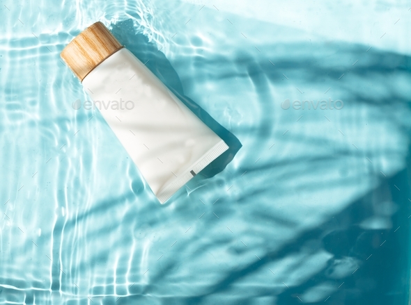 Beauty cosmetic lotion bottle in blue water with leaves shadow. Moisturizing beauty cream, skincare