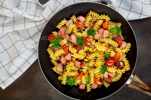 Colorful pasta rotini, cherry tomatoes and ham on pan. Close up. Top view.