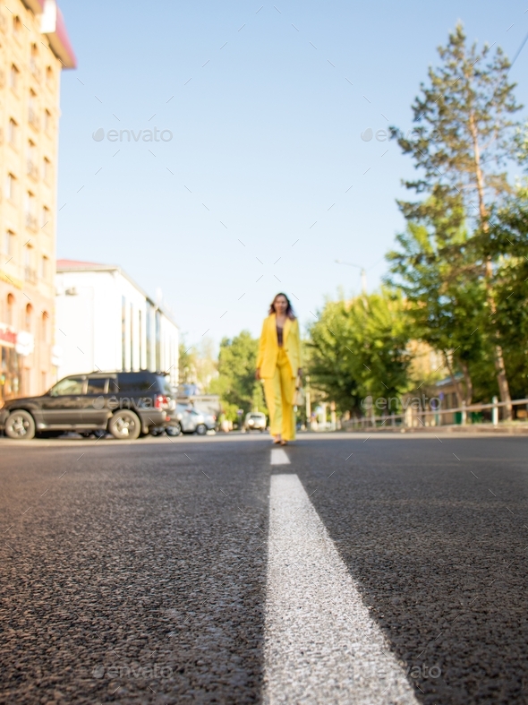 woman in a bright yellow trouser suit walks along the road markings on asphalt,