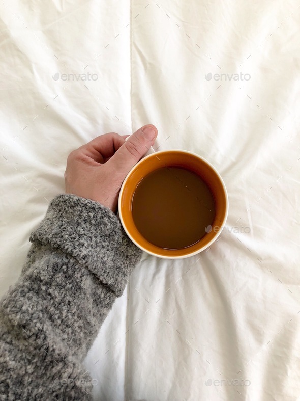 Hand holding cup of coffee on white comforter