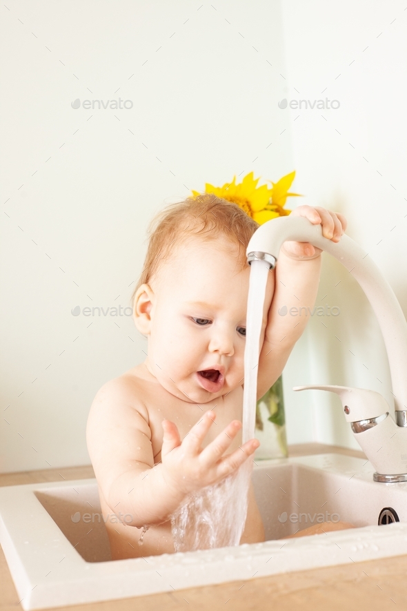 Baby taking bath in kitchen sink. Little boy bathing. Water fun for