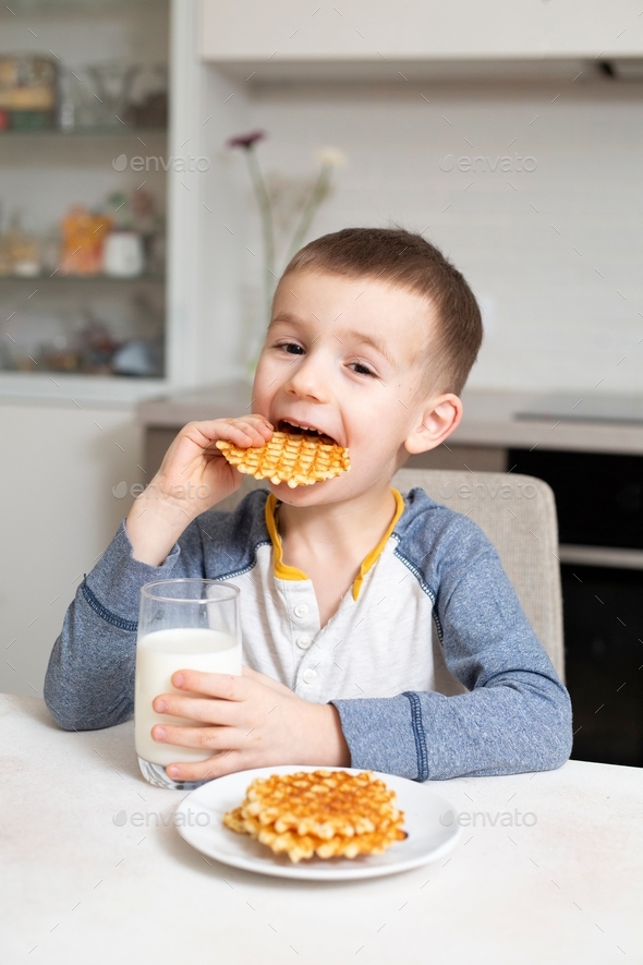 little boy eats waffles, holds a glass of milk in his hand Stock Photo