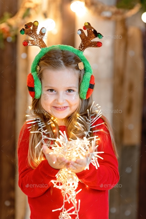 Happy smiling little girl holding Christmas lights and wearing fancy