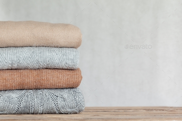 Stack of cozy knitted sweaters on a neutral background. Warm concept
