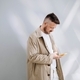Young man in a beige coat flips through the mobile feed and smiles. Vertical photo. Using technology - PhotoDune Item for Sale