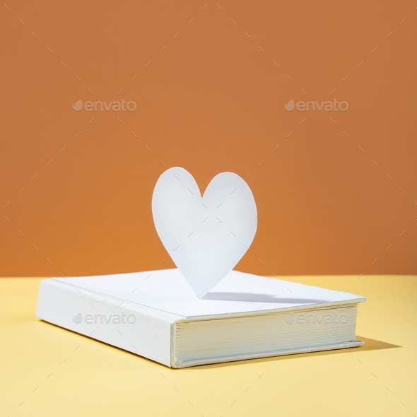 Floating Cute paper heart and white cover book on bold color yellow and orange-brown background