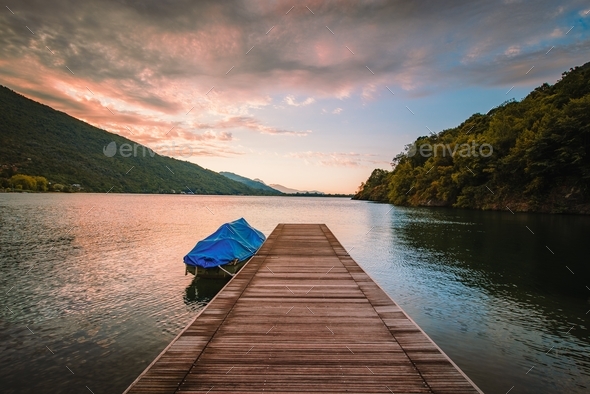 Lake Mergozzo at dawn with wooden jetty in the foreground and colored clouds. Without people