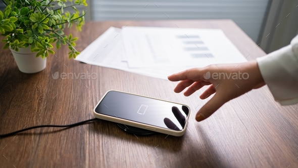 Charging mobile phone battery with wireless charging device in the table. Smartphone