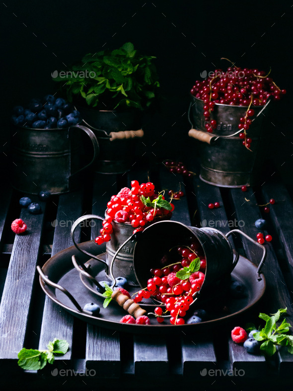 berries currants blueberries raspberries basil in metal dishes in buckets on a wooden dark board - Stock Photo - Images