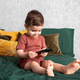 A toddler boy using mobile phone and sits on green bed  in bedroom . Kids and technology,happy smile - PhotoDune Item for Sale