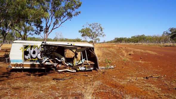 Destroyed caravan/mobile home on side of remote dirt road, medium shot pan alt