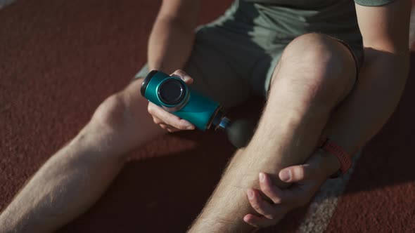 A Male Athlete Massages Muscles and Tendons with a Massage Percussion Device After a Workout at the alt