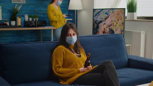 Woman Relaxing with Friends Sitting on Couch Wearing Face Mask alt