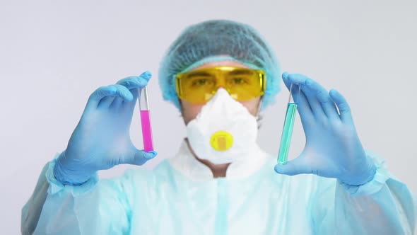 Laborant in Biohazard Suit Showing Two Sample of Antivirus To Covid-19 alt