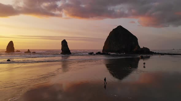 People Walk Cannon Beach as Pacific Ocean Waves Reflect Sunset Glow