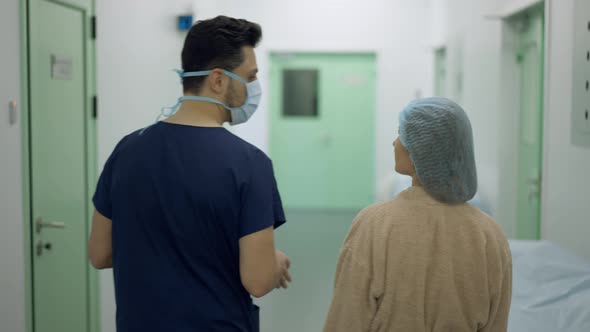 Back View of Doctor and Patient Walking to Operating Room in Clinic Talking in Slow Motion alt