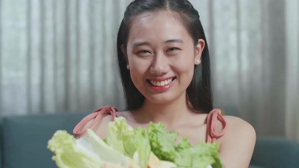Close Up Of Smiling Asian Woman Showing A Dish Of Healthy Food To Camera While Sitting At Home alt