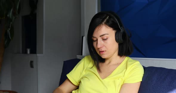 Woman in casual clothes put on headphones and click on smartphone, listening to podcast alt