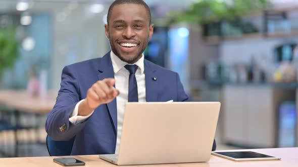 African Businessman with Laptop Pointing at the Camera  alt