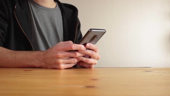 Young man using dark grey smartphone, texting and scrolling. alt