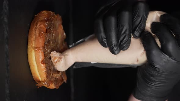 Hand of the chef in black rubber gloves pouring Foie on a gourmet burger. Preparation of a burger in alt