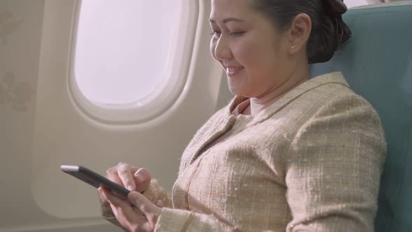 Asian female passenger sitting at seat using mobile phone alt