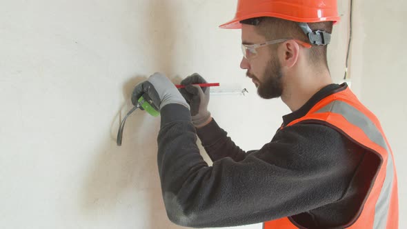 Bearded Male Contractor Measuring and Drilling Wall