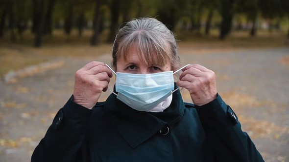 Portrait of a Senior Woman Putting on a Medical Mask and Looking Seriously at the Camera.