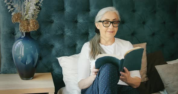 Elderly Woman Reading Book on Sofa