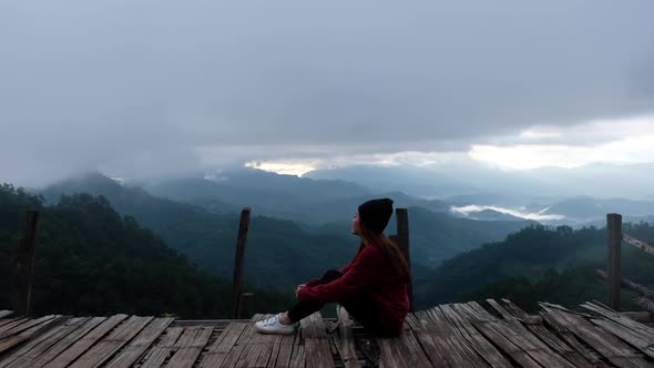 Slow motion of a female traveler sitting and looking at a beautiful mountains view on foggy day