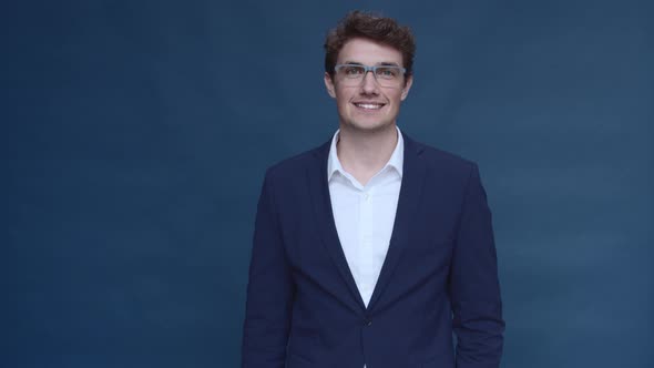 Model in Business Attire Standing in Front of Blue Backdrop Smiling alt