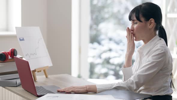 Side View of Positive Smiling Young Slim Businesswoman Sending Air Kisses at Laptop Sitting Indoors alt