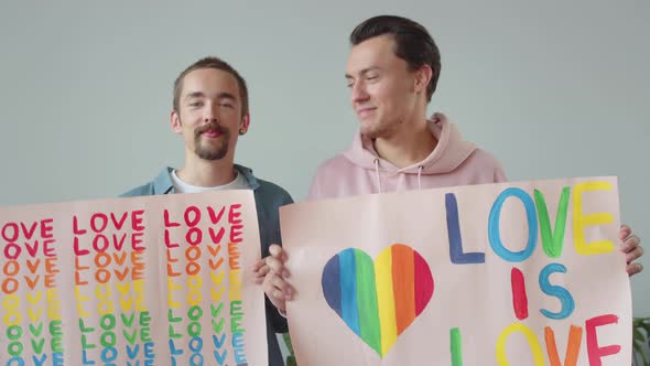 Two Young Men are Showing Lgbt Posters Looking at Each Other and Smiling alt