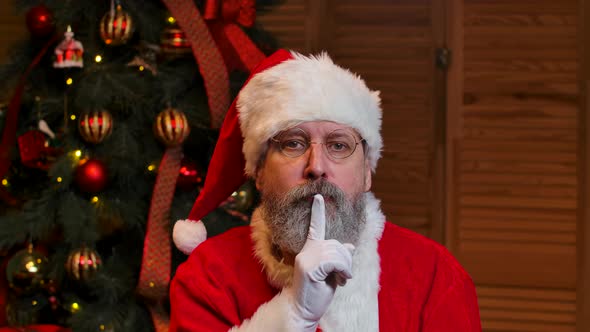 Portrait of Santa Claus Looking Pensively Around Makes Secret Gesture and Winks alt