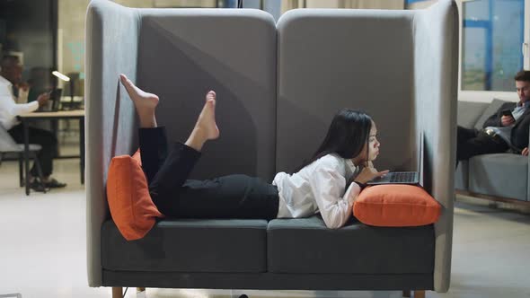Asian Female Office Manager Lies in a Large Chair and Works at a Laptop Working in an International alt